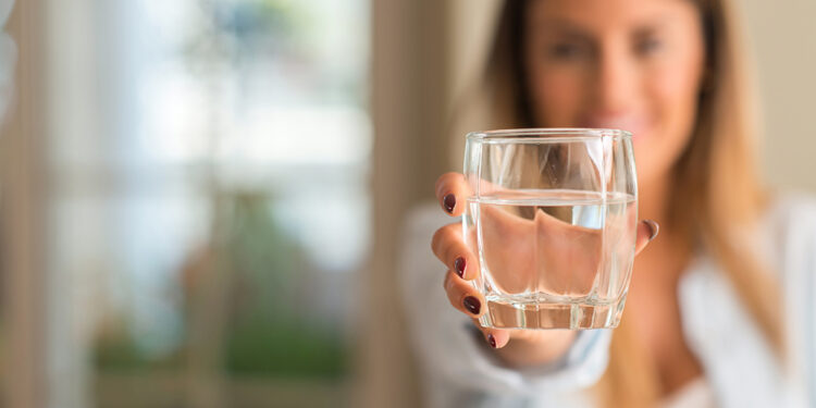 Beautiful young woman smiling while holding a glass of water at